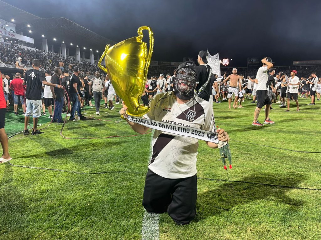 Torcedor vestido de macaco segurando uma faixa de campeão e um troféu de balão