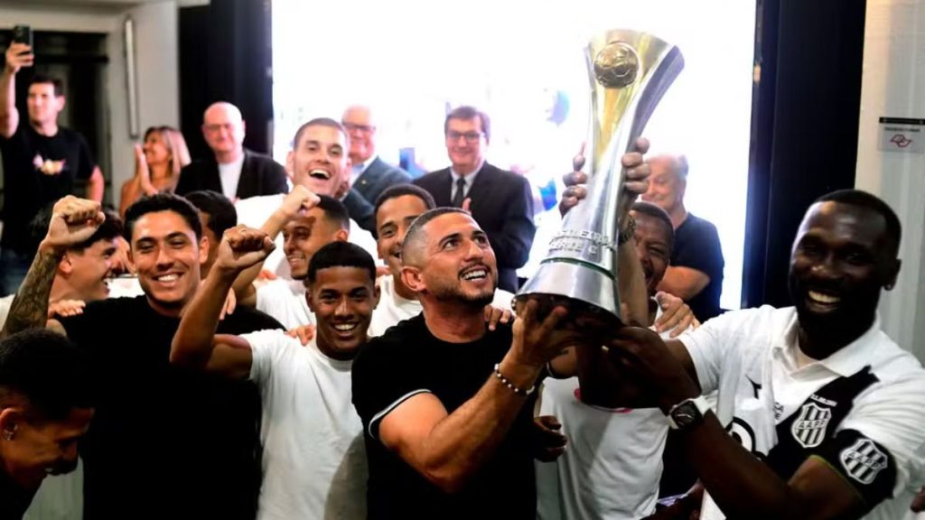 Jogadores da Ponte Preta reunidos comemorando e segurando a taça de campeão da Série C