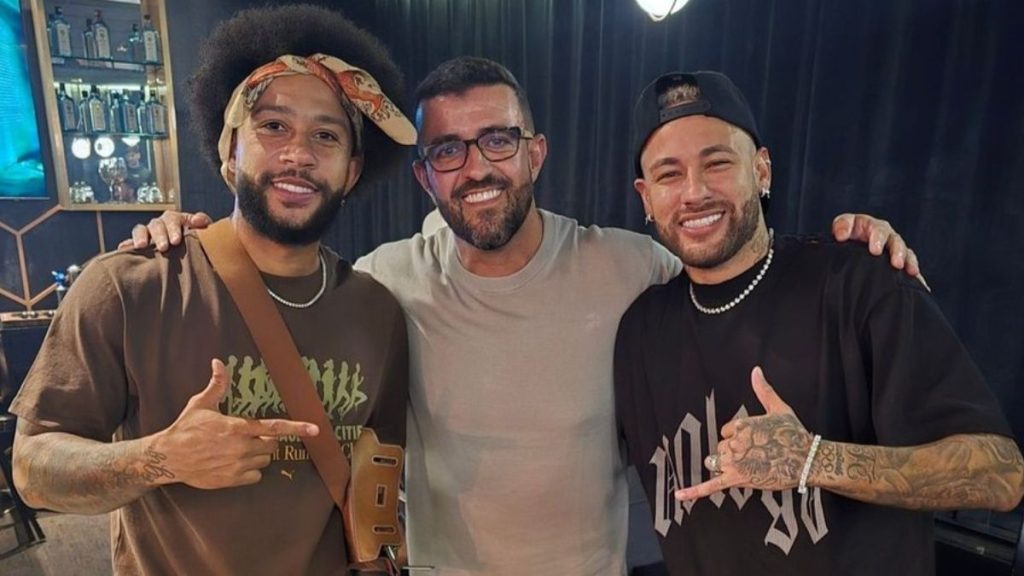 André Akkari ao centro entre os jogadores Memphis Depay e Neymar em registro de encontro amigável.