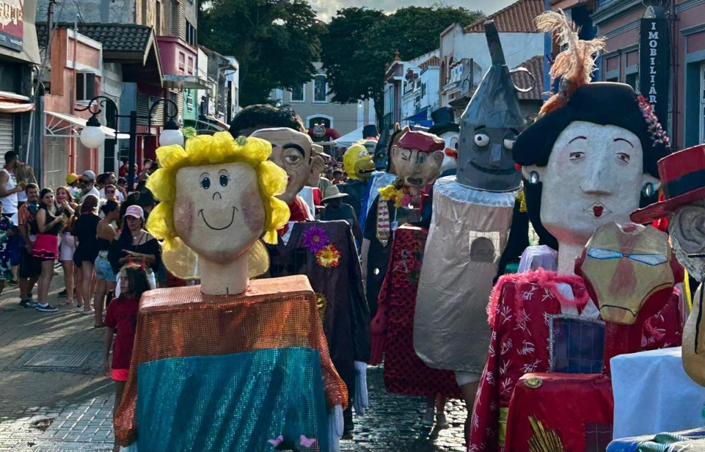 Bonecões gigantes e coloridos desfilando entre foliões nas ruas históricas durante o Carnaval em Atibaia.