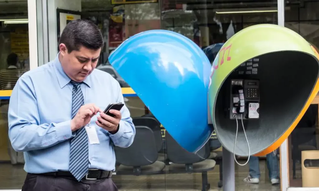 Orelhão de telefonia pública em calçada urbana, simbolizando a remoção dos aparelhos das ruas brasileiras.