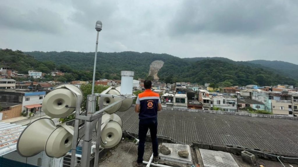 Sirene de alerta na Comunidade Barreira do João Guarda em Guarujá após deslizamentos causados por fortes chuvas.