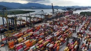 Vista aérea do terminal de contêineres no Porto de Santos com navios cargueiros e guindastes de carga.