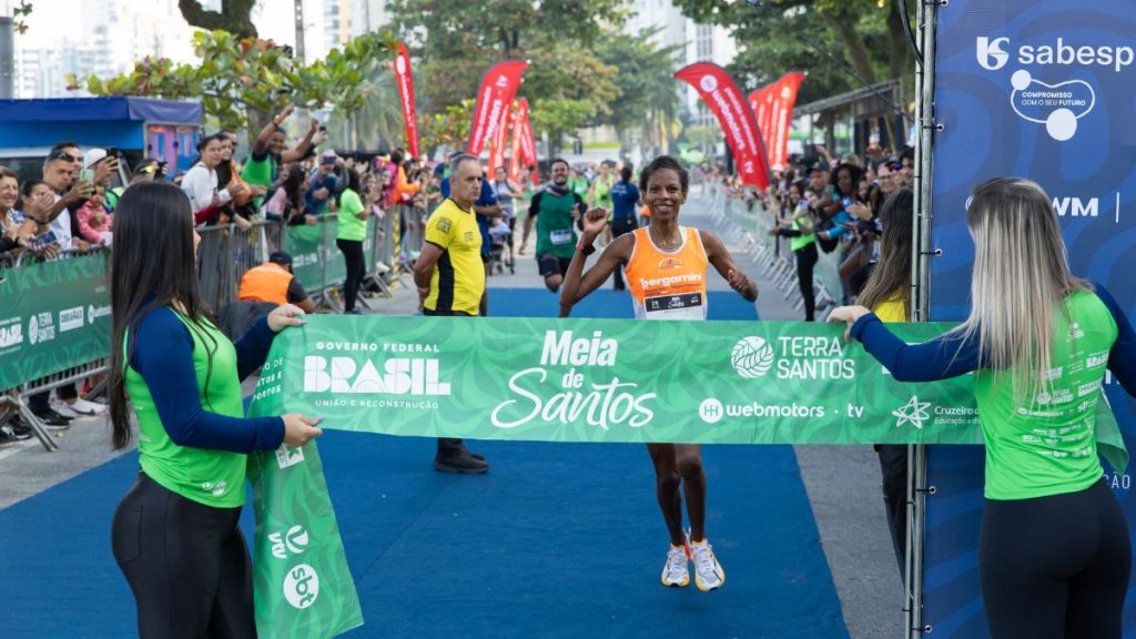 Corredores em largada da Meia de Santos 2026 destacando percursos de 7km e 21km no litoral.