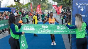 Corredores em largada da Meia de Santos 2026 destacando percursos de 7km e 21km no litoral.