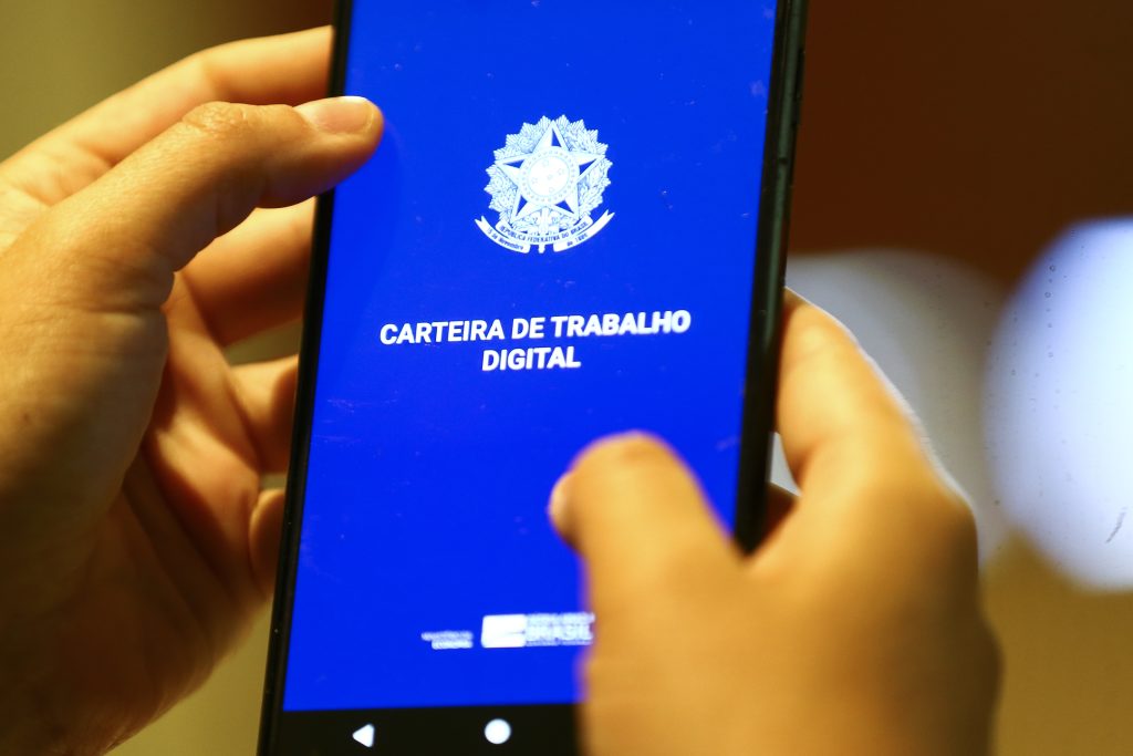 Smartphone com aplicativo Carteira de Trabalho Digital em destaque sobre recorde de registro na previdência social.