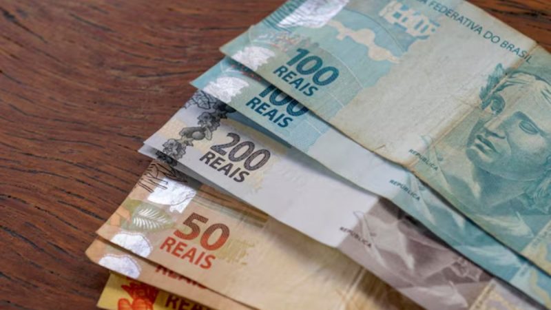 Aposentado manuseando cédulas de Real e cartão do INSS, simbolizando a antecipação do 13º salário.