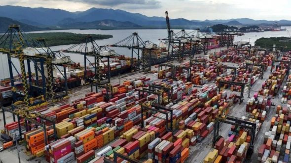 Vista aérea do terminal de contêineres no Porto de Santos com navios cargueiros e guindastes de carga.