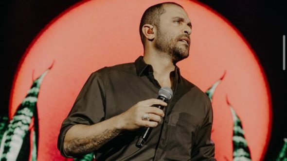 Cantor Diogo Nogueira sorrindo durante show ao vivo interpretando o sucesso Pé na Areia em evento.