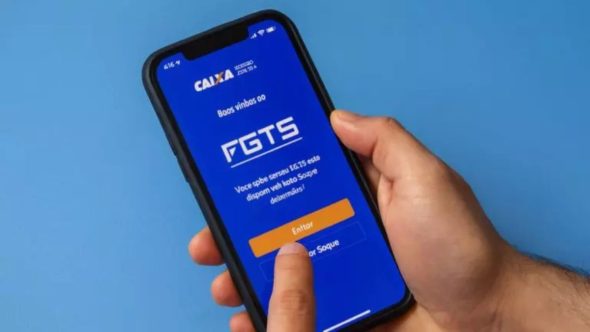 Trabalhador consultando calendário do abono salarial PIS-PASEP em smartphone com carteira de trabalho.