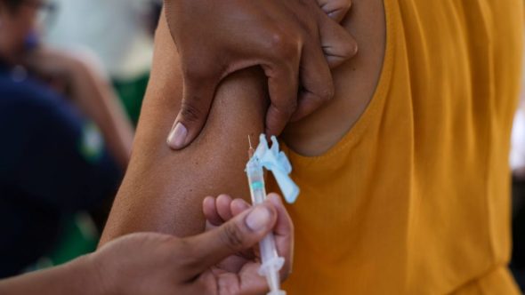 Profissional de saúde aplica vacina para mitigar alerta sobre sarampo na Copa do Mundo 2026 e proteger a população.