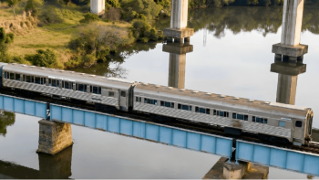 Locomotiva a vapor percorrendo paisagem natural em passeio ferroviário turístico nostálgico.