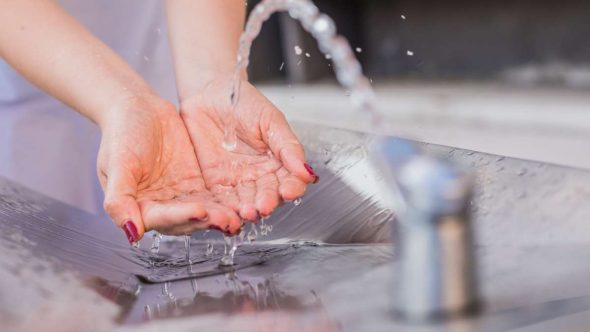 Mãos fechando torneira para promover economia de água e gestão sustentável de recursos durante a temporada de seca.