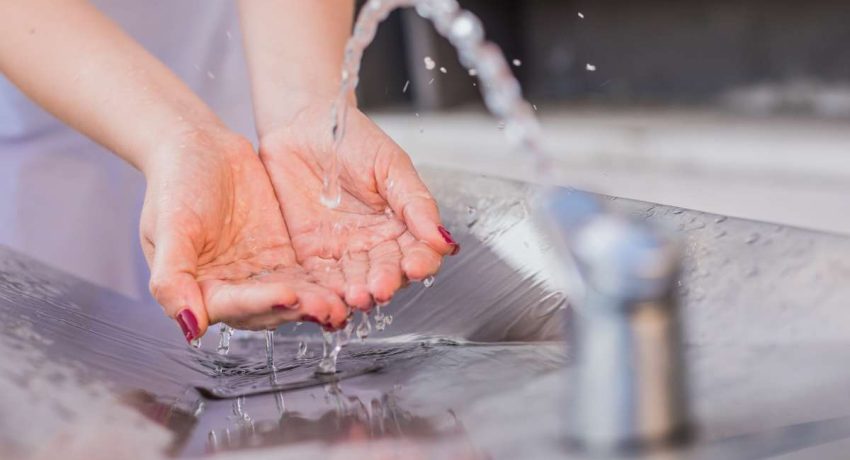 Mãos fechando torneira para promover economia de água e gestão sustentável de recursos durante a temporada de seca.