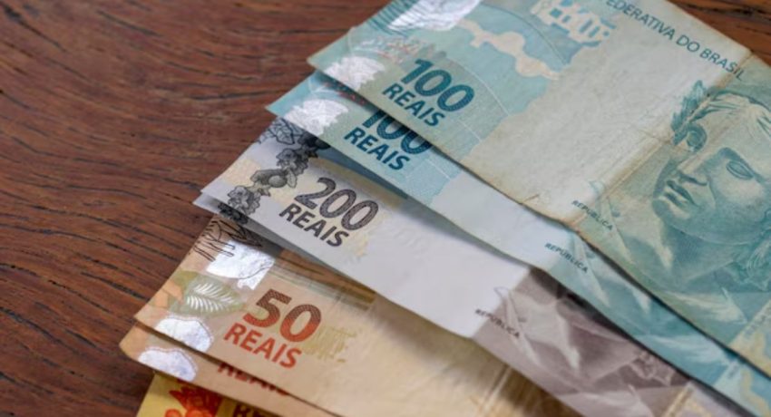 Aposentado manuseando cédulas de Real e cartão do INSS, simbolizando a antecipação do 13º salário.