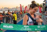 Corredora amamentando bebê em preparação para a 8ª Meia de Santos, unindo esporte e maternidade.